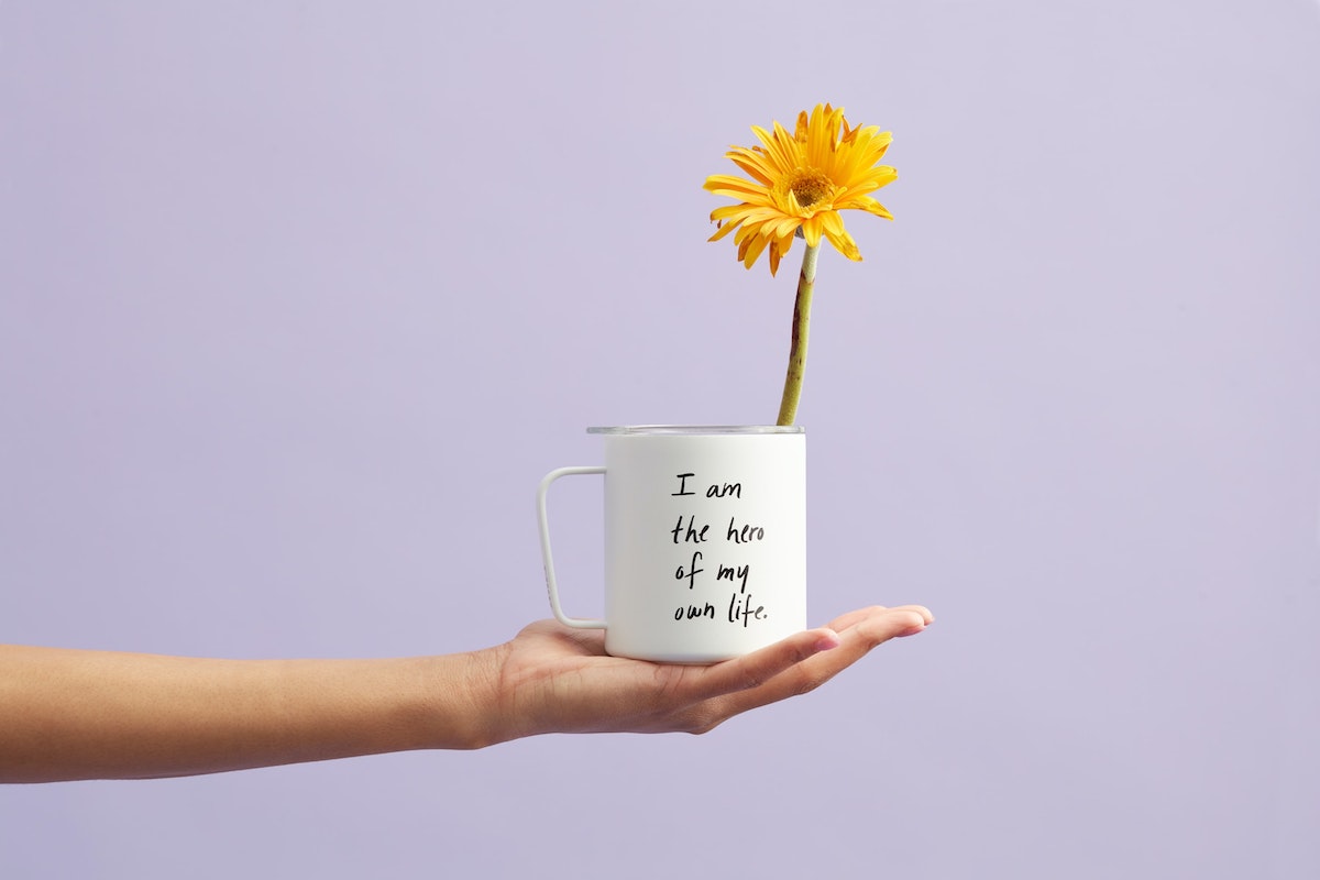Career Success. Putting Your Strengths to Work. A Self-Assessment Guide. Mug in a hand with message I am the hero of my own life with sunflower in the mug