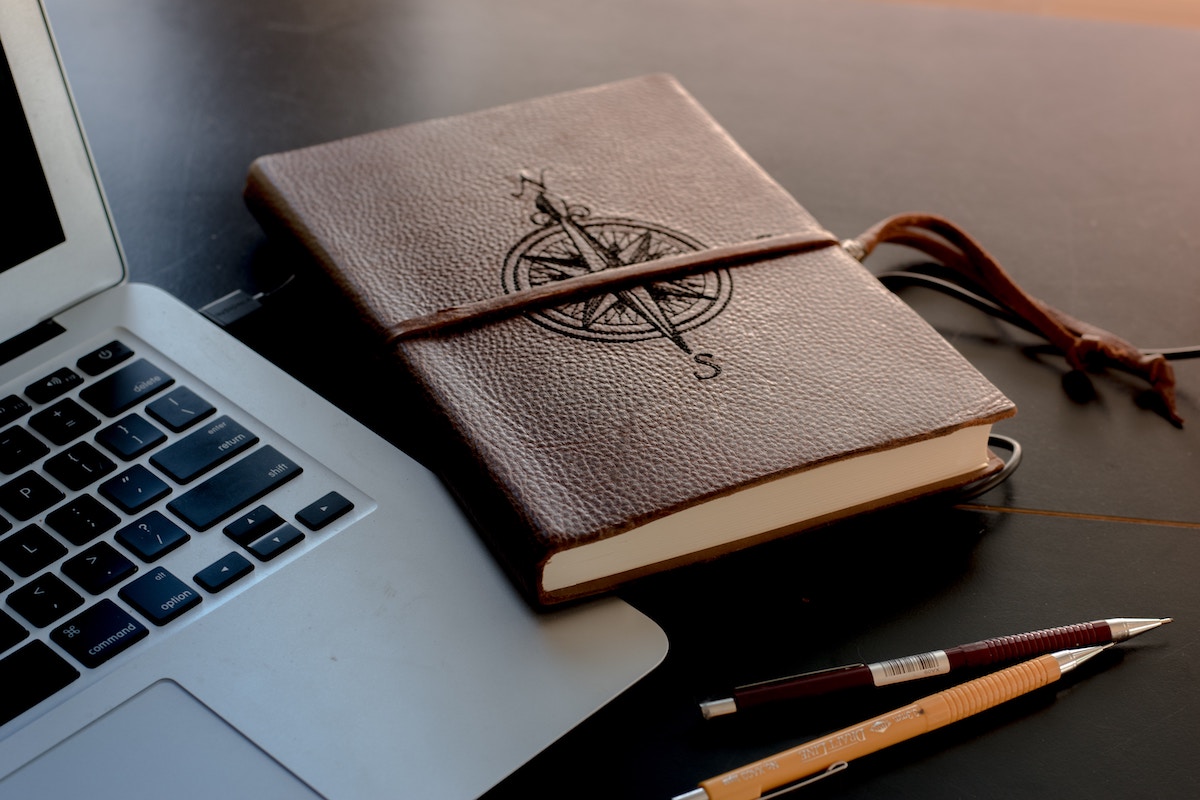 Picrture of a laptop and a note book with a compass on the front for our Navigating the First 90 Days in a New Role: Tips for Professional Success blog