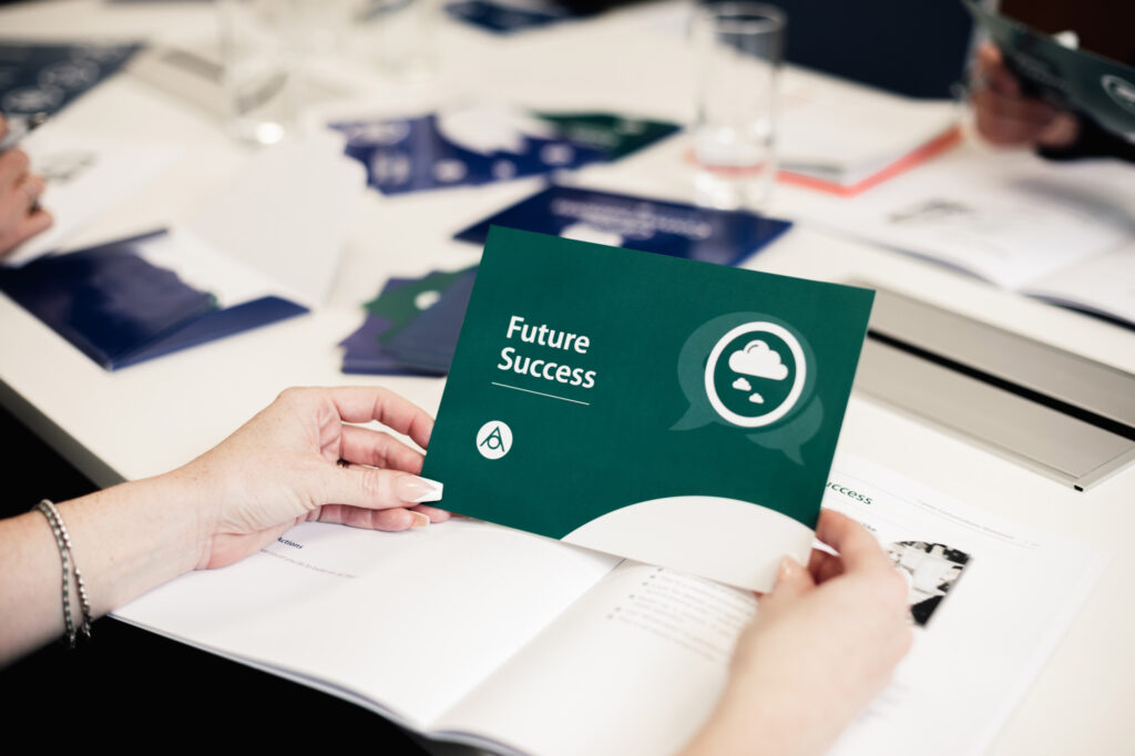 A person holding a green card that reads "Future Success" from Antoinette Oglethorpe's Career Conversation Toolkit at a table with open documents and scattered papers, in a business meeting