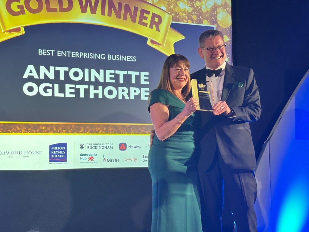 Two people in formal attire smile and hold a trophy on stage under a banner reading 