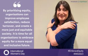 A woman with shoulder-length brown hair, wearing a blue top, smiles and hugs herself. Beside her is a quotation about embracing equity for a just and inclusive workplace. International Women's Day and equity hashtags are shown.
