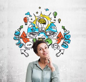 A thoughtful woman stands in front of a wall with colourful doodles of a lightbulb, arrows, clouds, and the words “PLAN” and “IDEA”, symbolising creativity and brainstorming.