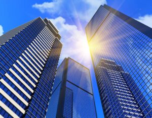 Tall glass skyscrapers reflecting sunlight and blue sky with clouds, viewed from below. Bright sunlight shines between the buildings, symbolising career development in a modern urban cityscape.