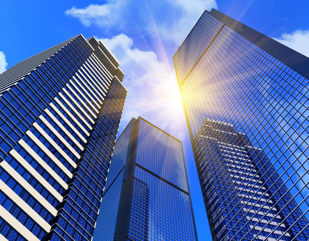 Tall glass skyscrapers reflecting sunlight and blue sky with clouds, viewed from below. Bright sunlight shines between the buildings, symbolising career development in a modern urban cityscape.