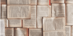 A collection of open books laid out overlapping each other, displaying various pages filled with text in different typefaces and orientations. The books create a textured, literary background that evokes the spirit of positive mentoring and shared knowledge.