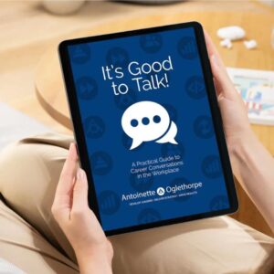 A woman sits on a sofa holding a tablet displaying a blue cover titled “It’s Good to Talk! A Practical Guide to Career Conversations in the Workplace” by Antoinette at Oglethorpe, with a chat bubble icon in the centre.